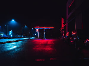 Neon-lit gas station at night with red and blue lights reflecting on wet asphalt HD wallpaper