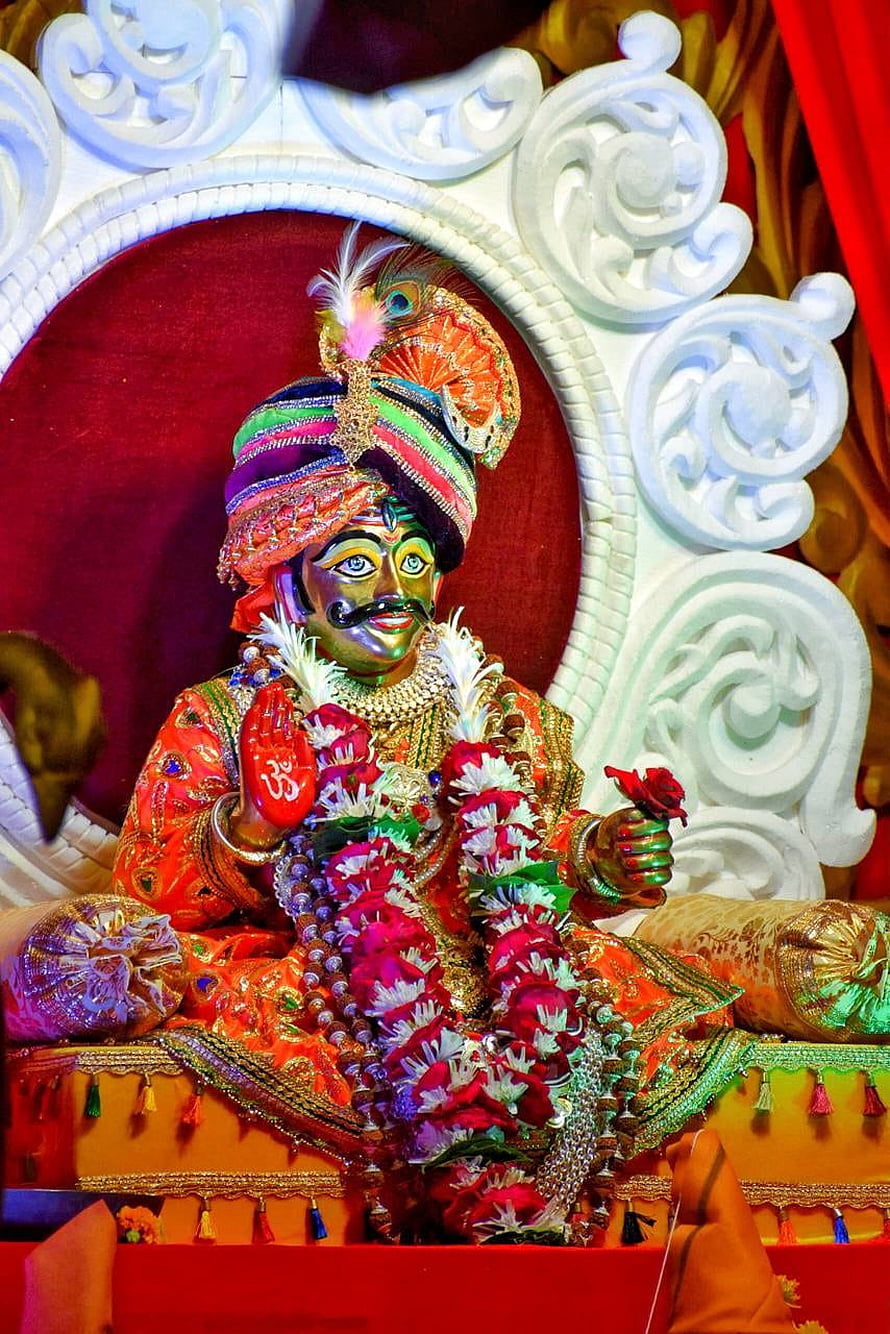 Colorful Statue of Lord Krishna with Peacock Feather Crown and Floral Garlands HD phone wallpaper