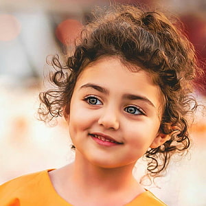 Portrait of a young girl with curly brown hair and a gentle smile HD phone wallpaper