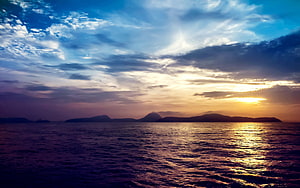 Golden sunset over a calm sea with distant island silhouettes and dramatic clouds HD wallpaper