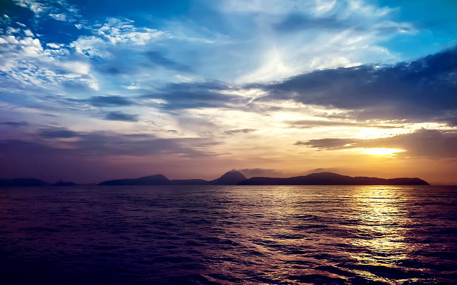 Golden sunset over a calm sea with distant island silhouettes and dramatic clouds HD wallpaper