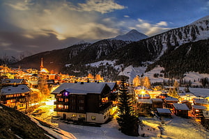 Alpine Village at Dusk with Snow-Covered Chalets and Mountain Peaks HD wallpaper