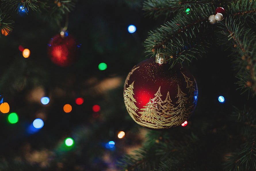 Red Christmas Ornament with Gold Tree Design Hanging on Pine Branch with Colorful Bokeh Lights HD wallpaper