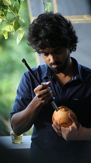 GV Prakash Opening A Coconut With A Tool In A Natural Setting HD phone wallpaper