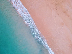 Aerial View of Turquoise Ocean Waves Lapping Against Pink Sand Beach HD wallpaper