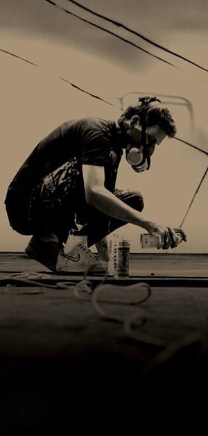 Sepia-Toned Graffiti Artist Crouching with Spray Paint Can and Respirator Mask HD phone wallpaper