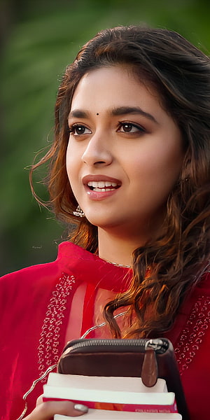 Keerthy Suresh in a red embroidered outfit holding books with a warm smile HD phone wallpaper