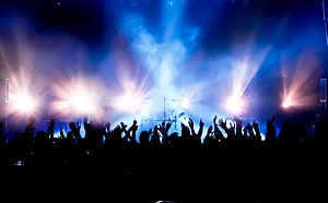 Silhouetted concert crowd with raised hands under dramatic blue stage lighting and smoke HD wallpaper