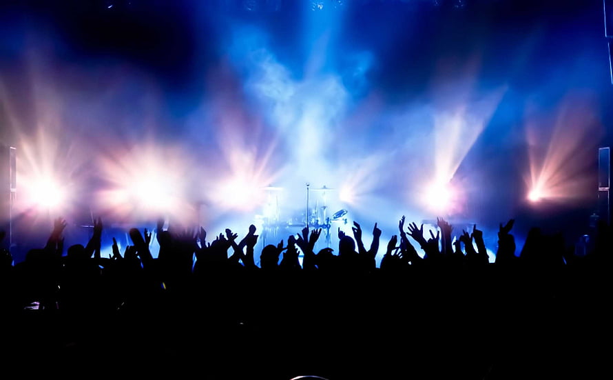 Silhouetted concert crowd with raised hands under dramatic blue stage lighting and smoke HD wallpaper