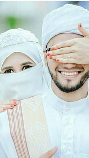 Smiling Muslim Couple in Traditional White Attire with Hijab and Cap HD phone wallpaper