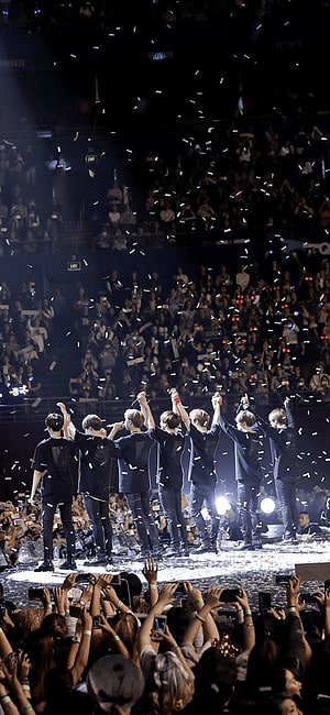 BTS performing on stage with arms raised during a concert with falling confetti and cheering fans HD phone wallpaper