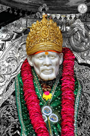 Statue of Sai Baba adorned with golden crown and red flower garlands HD phone wallpaper