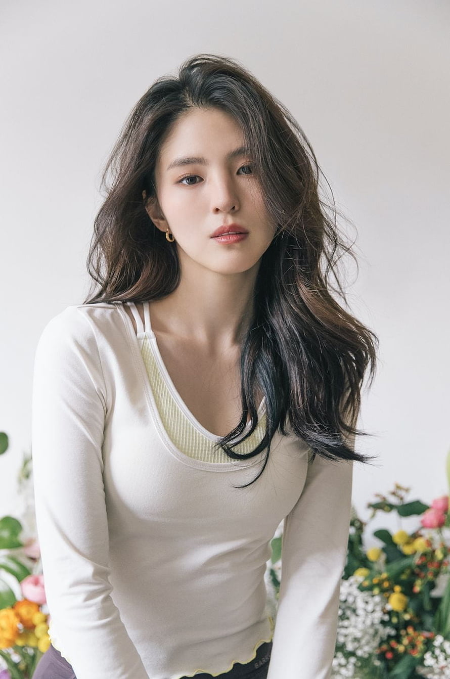 Portrait of a woman with long wavy hair wearing a white top surrounded by colorful flowers, The World of The Married Actress Han So Hee Began Acting For One Reason And One Reason Only HD phone wallpaper