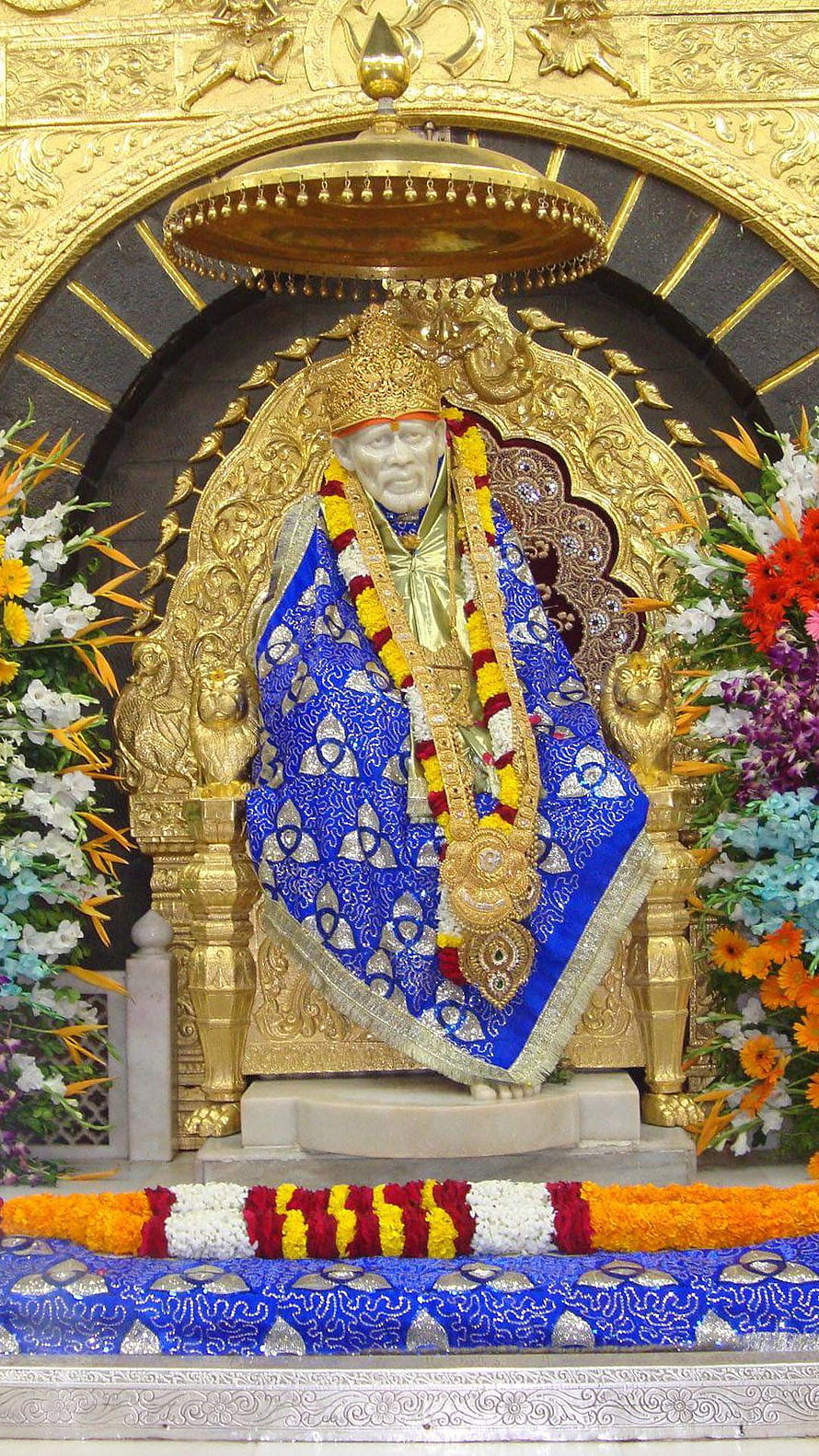 Sri Sathya Sai Baba Statue in Blue Robes with Golden Crown and Flower Garlands HD phone wallpaper