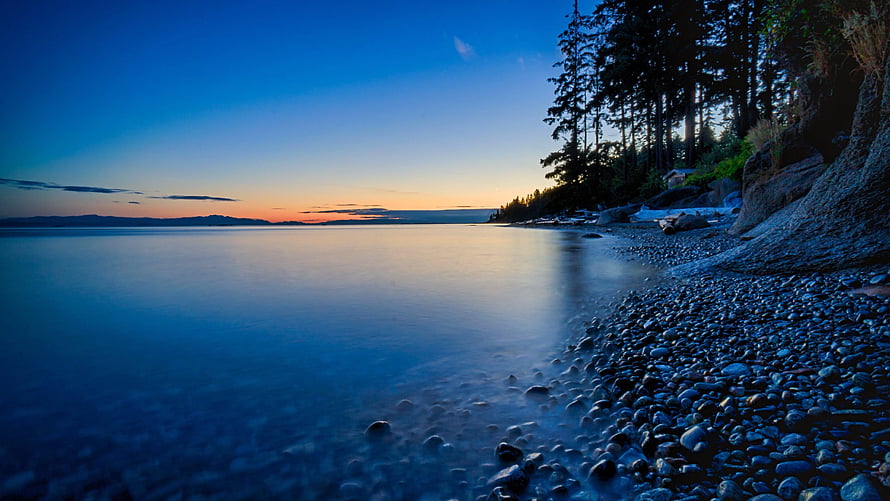 Serene Twilight at a Rocky Lake Shore with Pine Forest and Smooth Water Reflections HD wallpaper