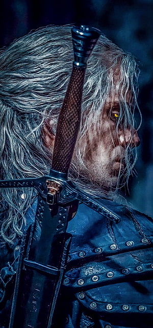Geralt of Rivia from The Witcher with sword and glowing yellow eyes in dark leather armor HD phone wallpaper