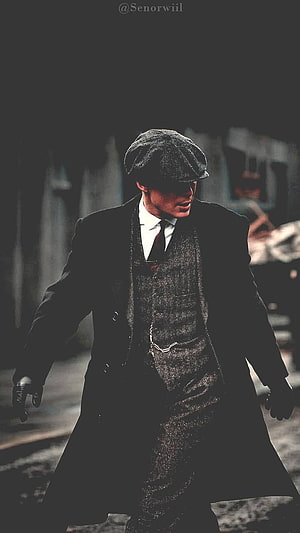 Tommy Shelby in Peaky Blinders wearing a flat cap and dark overcoat in a moody industrial setting HD phone wallpaper