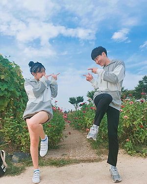 Korean couple posing playfully in a flower garden under a bright blue sky HD phone wallpaper