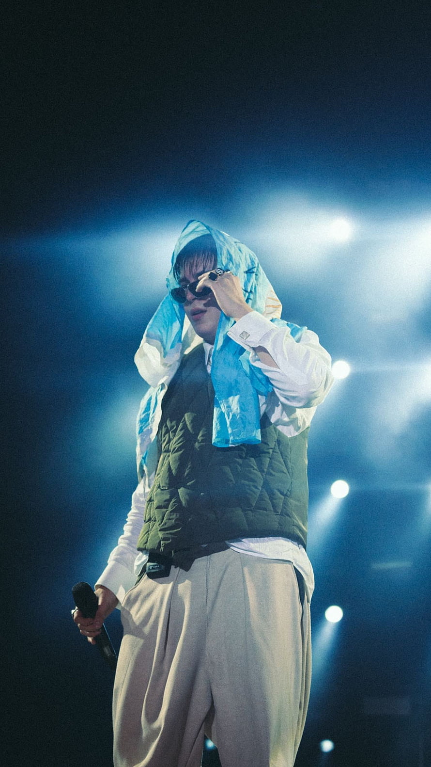 Male performer on stage in a blue hooded jacket and sunglasses holding a microphone under bright concert lights HD phone wallpaper