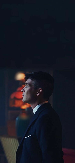 Tommy Shelby from Peaky Blinders in a dark suit looking up in a dimly lit room HD phone wallpaper
