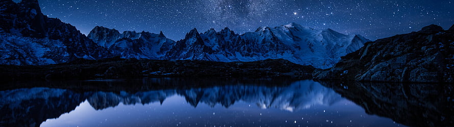 Snow-Capped Mountain Range Reflected in a Calm Alpine Lake Under a Starry Night Sky HD wallpaper