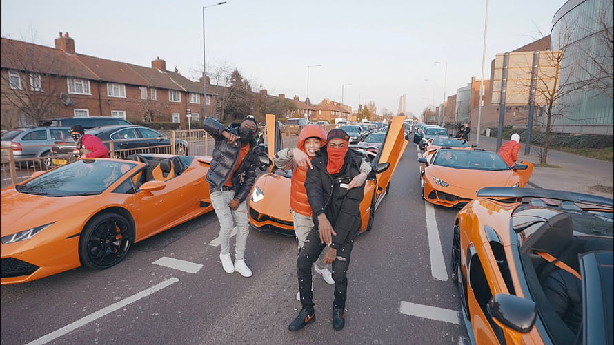 Central Cee posing with friends in a street lined with orange Lamborghini supercars HD wallpaper