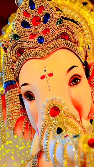 Close-up of Lord Ganesha adorned with a jeweled crown and intricate decorations HD phone wallpaper