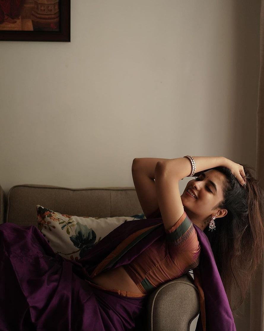 Priyanka Mohan in a purple saree reclining on a sofa with floral cushion HD phone wallpaper