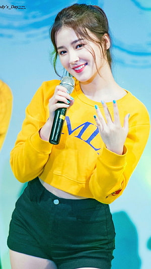 Nancy from Momoland performing on stage in a yellow sweatshirt and black shorts holding a microphone HD phone wallpaper