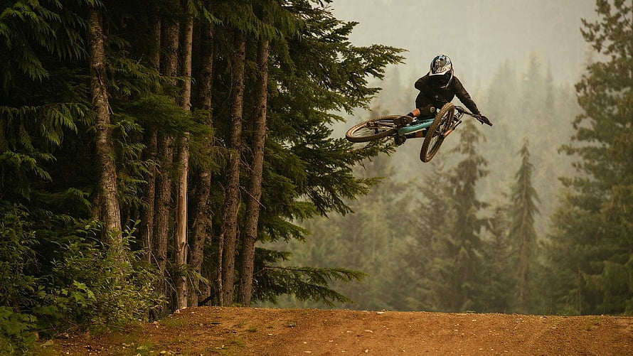 Mountain Biker Mid-Air Jump Over Forest Trail in Misty Pine Woods HD wallpaper