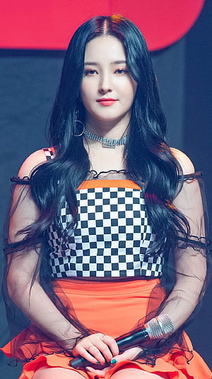 Nancy from Momoland in a stylish black and white checkered top with orange skirt holding a microphone HD phone wallpaper