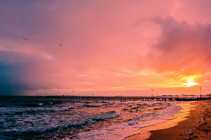 Vibrant Pink and Orange Sunset Over a Long Pier Extending Into the Ocean HD wallpaper