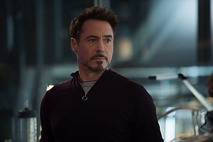 Tony Stark in a dark zip-up sweater with a serious expression in a modern industrial setting HD wallpaper