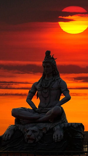 Statue of Hindu God Shiva Sitting in Meditation Pose Against Vibrant Orange Sunset Sky HD phone wallpaper