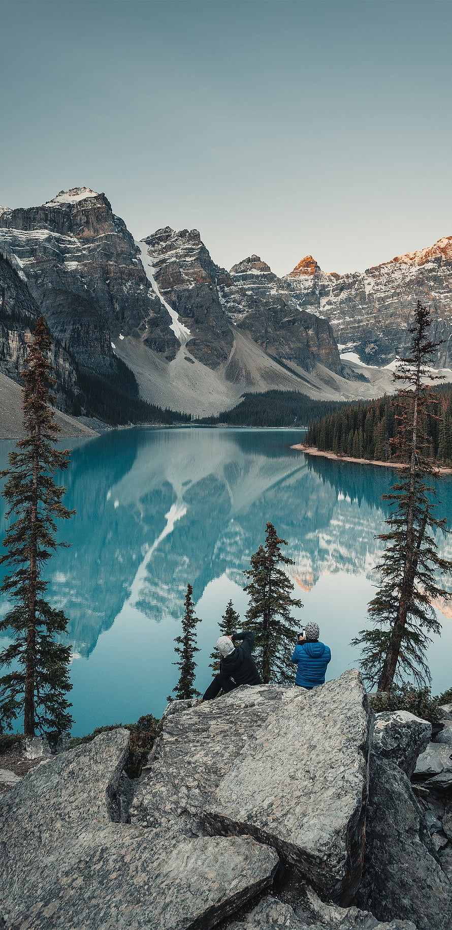 Two Hikers on Rocky Outcrop Overlooking Turquoise Mountain Lake with Perfect Reflections HD phone wallpaper