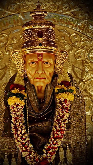 Golden Statue of Sai Baba Adorned with Flower Garlands and Ornate Crown HD phone wallpaper