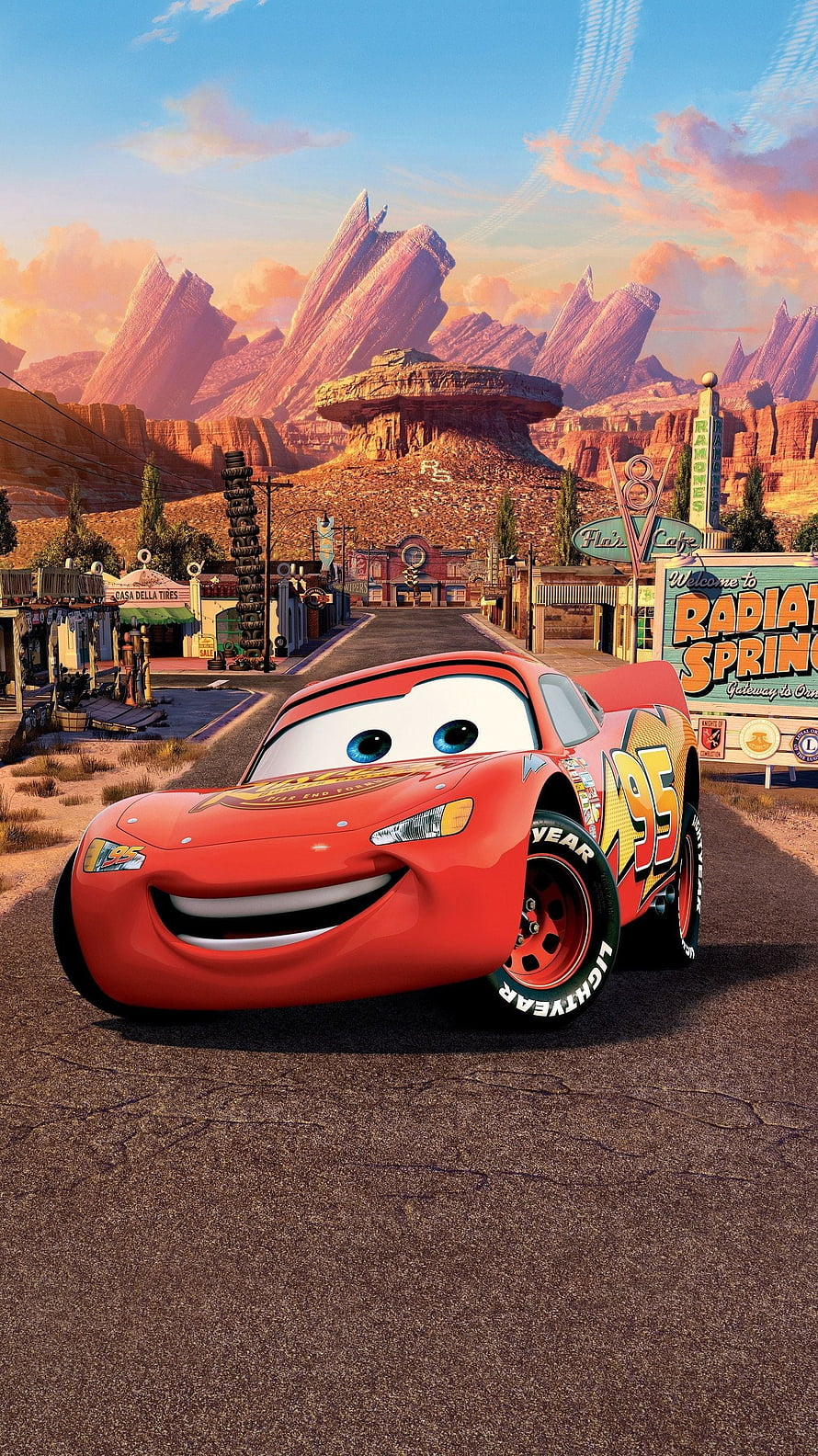 Lightning McQueen smiling on the road in Radiator Springs with desert mountains and sunset sky background HD phone wallpaper