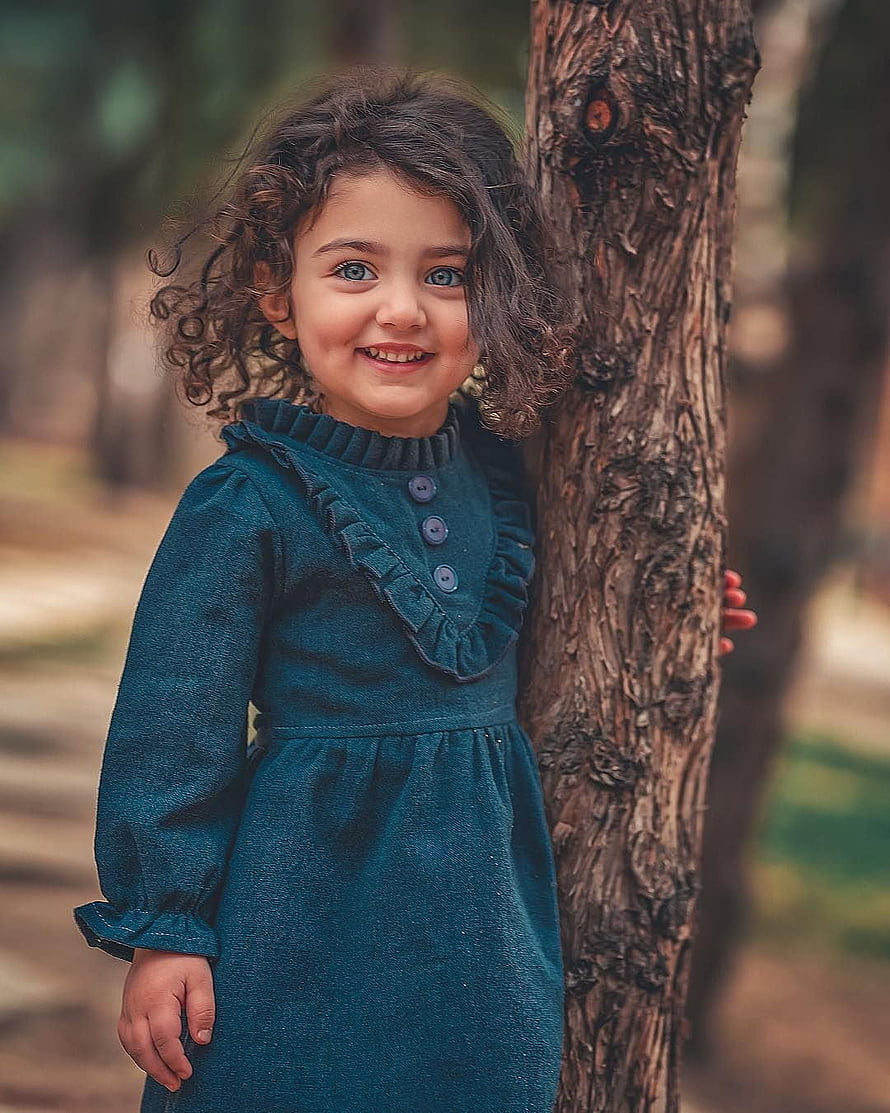 Cute Little Girl With Curly Hair Wearing A Teal Dress Standing By A Tree HD phone wallpaper