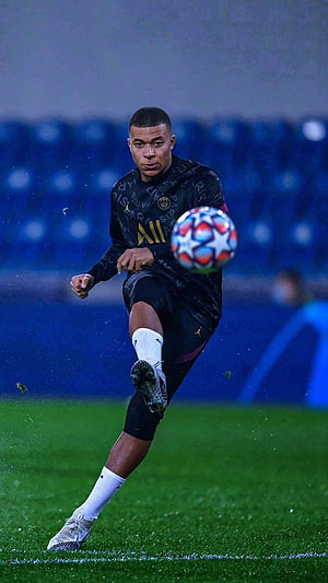 Kylian Mbappe in PSG kit striking a Champions League ball on a rainy night pitch HD phone wallpaper