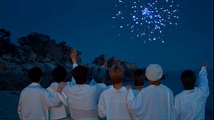 BTS members watching fireworks on a beach at night in white outfits HD wallpaper