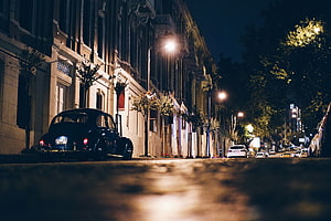 Vintage Black Car Parked on a Quiet Street at Night with Warm Streetlights HD wallpaper