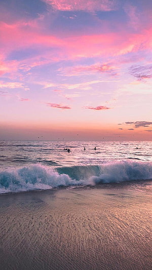 Pink Sunset Over Ocean Waves with Surfers on a Sandy Beach HD phone wallpaper