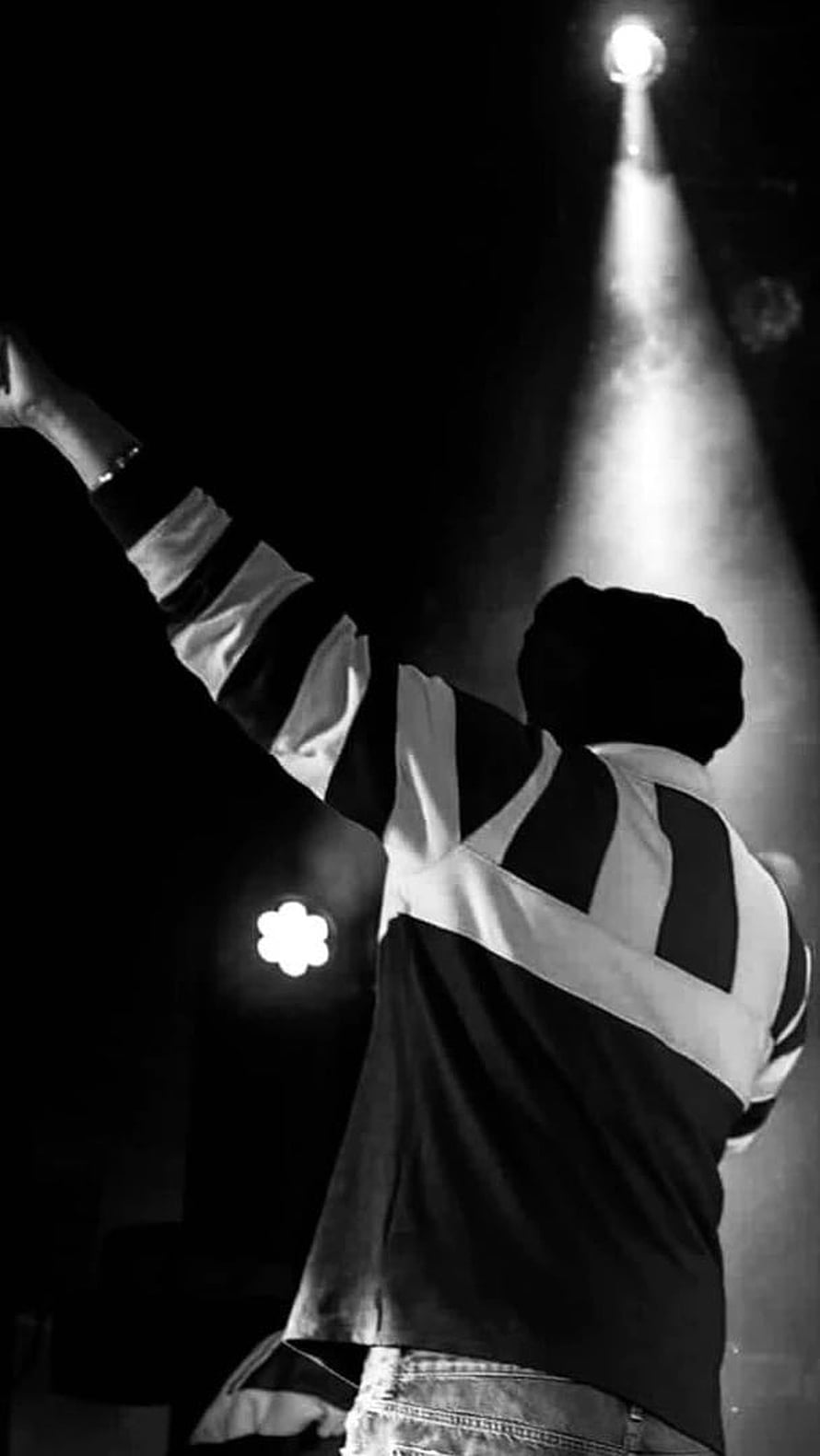Black and white photo of a person on stage with arm raised under spotlight HD phone wallpaper