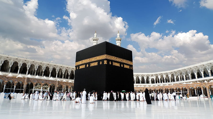 The Kaaba in Mecca with pilgrims performing tawaf under a bright blue sky HD wallpaper