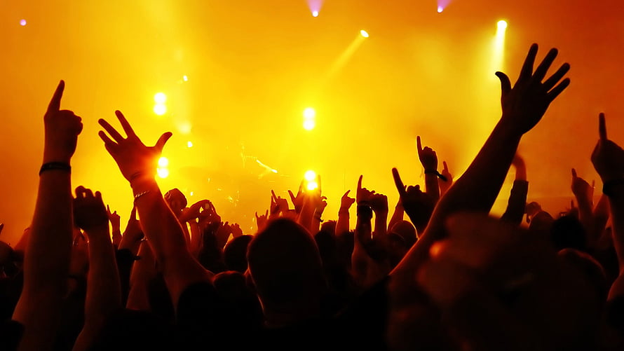 Silhouetted concert crowd with raised hands under golden stage lights HD wallpaper