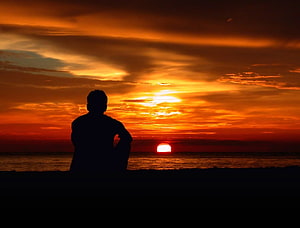 Silhouette of a Man Sitting on a Beach Watching a Vibrant Orange Sunset Over the Ocean, Lonely mood sad alone sadness emotion people loneliness Solitude, Sad Alone Man HD wallpaper