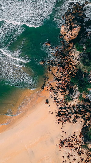 Aerial View of Turquoise Ocean Waves Crashing Against Rocky Coastline and Sandy Beach HD phone wallpaper