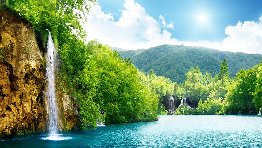 Serene turquoise lake surrounded by lush green forest and cascading waterfalls under a bright blue sky HD wallpaper