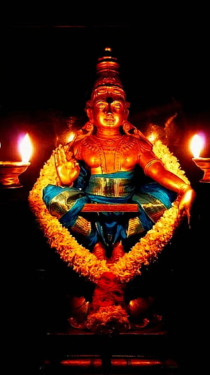 Ayyappa deity statue adorned with marigold garlands and oil lamps in a dark temple setting HD phone wallpaper