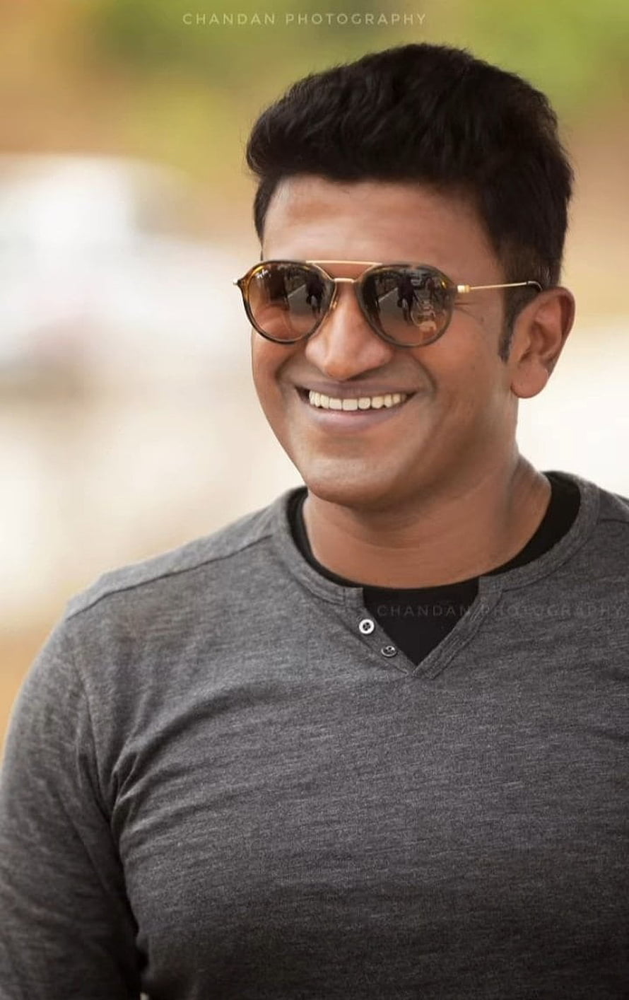 Puneeth Rajkumar smiling portrait wearing aviator sunglasses and a grey henley shirt HD phone wallpaper